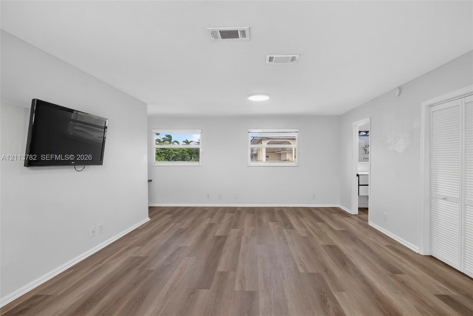 Neutral interior featuring wood-finish flooring, two dual-pane windows, and white bifold closet doors