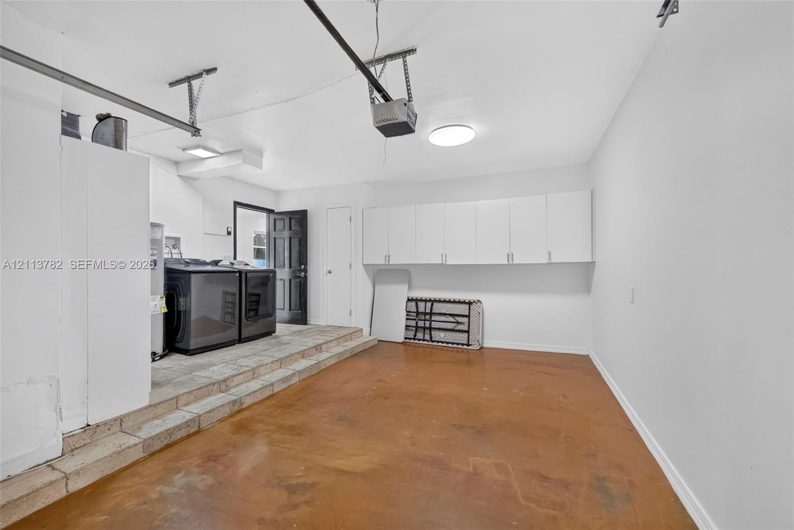 Garage featuring stained concrete flooring, white wall-mounted storage cabinetry, raised utility platform, and exterior access door