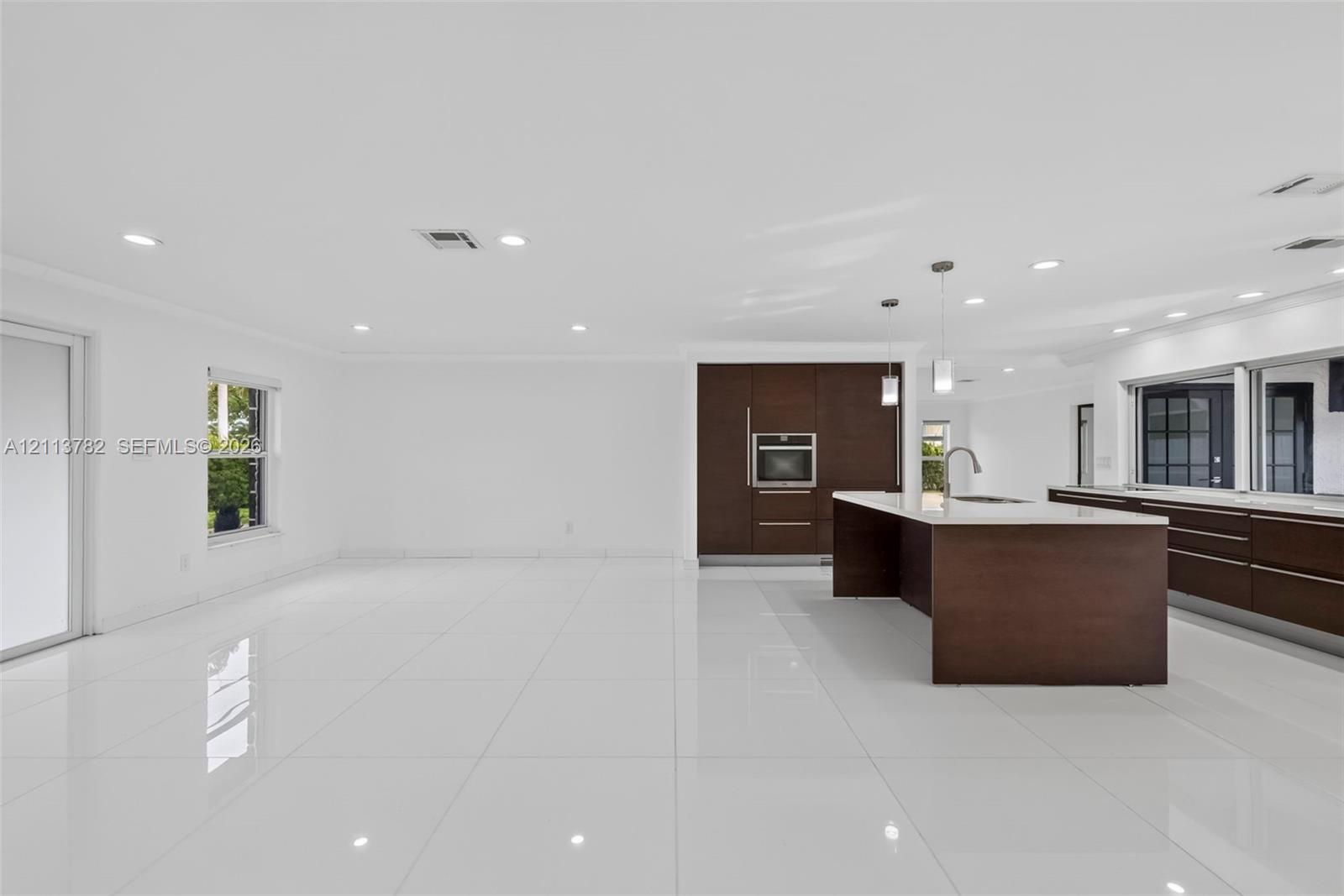 Open-concept kitchen featuring dark wood-finish cabinetry, a large center island with stone-surface countertop, recessed lighting, and white tile flooring throughout