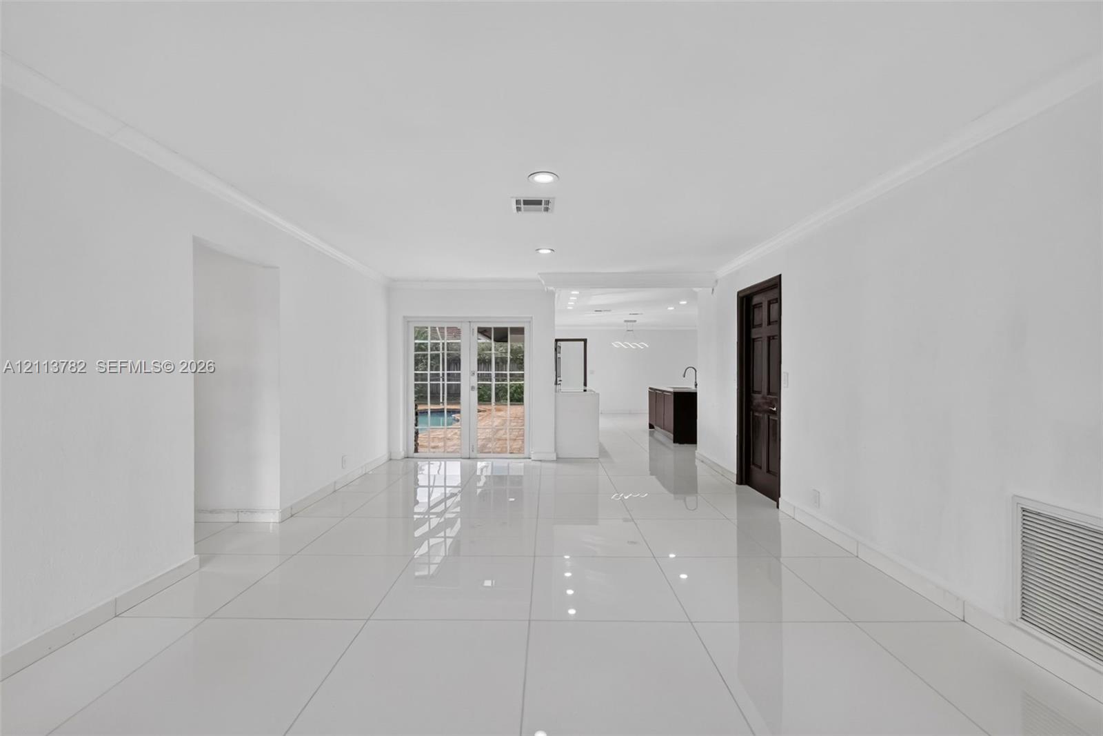 Open-concept room featuring large-format tile flooring, recessed lighting, and white-framed glass French doors