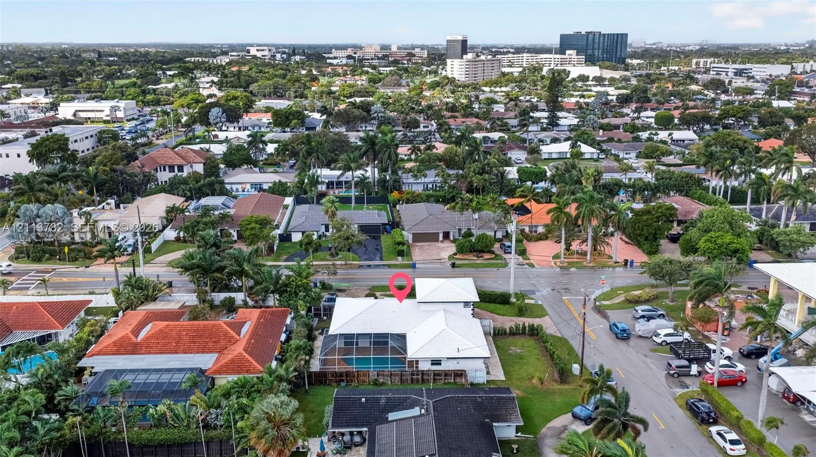 Aerial perspective featuring a white-roofed residence with a screen-enclosed pool, perimeter fencing, and established palm trees in a residential neighborhood