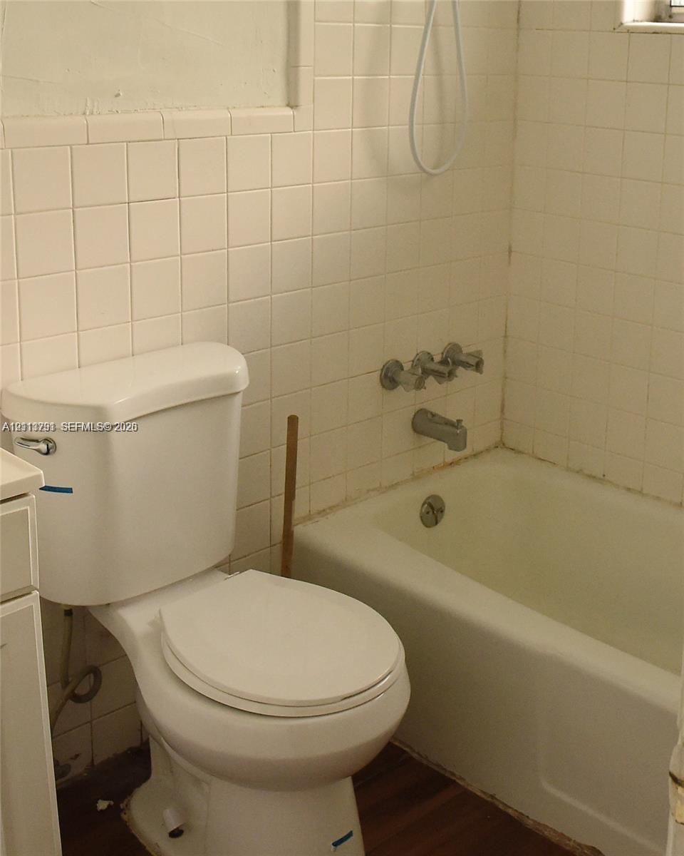 Bathroom featuring a white porcelain toilet, integrated bathtub and shower combination, and wall-mounted metallic fixtures Bathroom featuring a white porcelain toilet, integrated bathtub and shower combination, and wall-mounted metallic fixtures