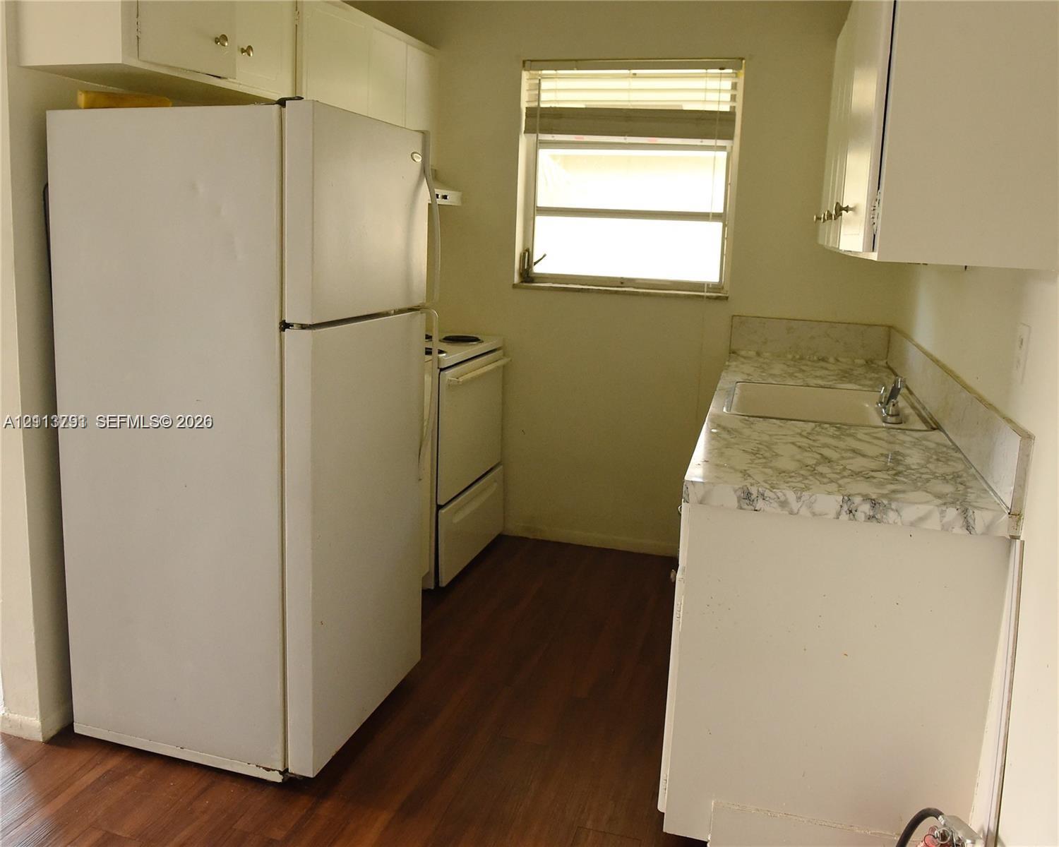 Kitchen featuring white cabinetry, patterned laminate countertops, a single-basin sink, wood-finish flooring, and a window Kitchen featuring white cabinetry, patterned laminate countertops, a single-basin sink, wood-finish flooring, and a window