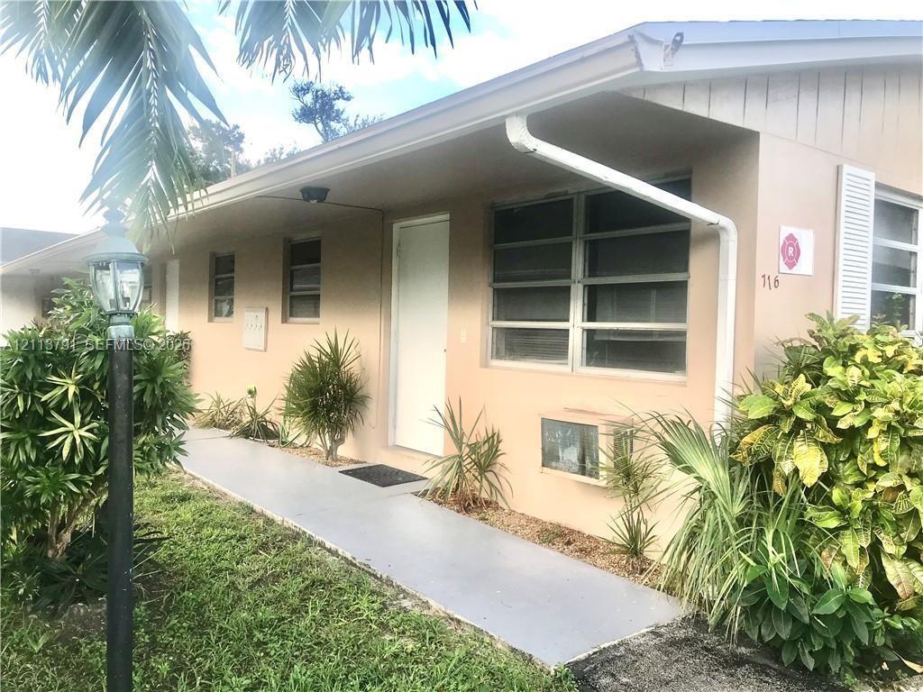 Stucco exterior featuring horizontal louvered windows, a covered concrete walkway, and an integrated exterior light post Stucco exterior featuring horizontal louvered windows, a covered concrete walkway, and an integrated exterior light post