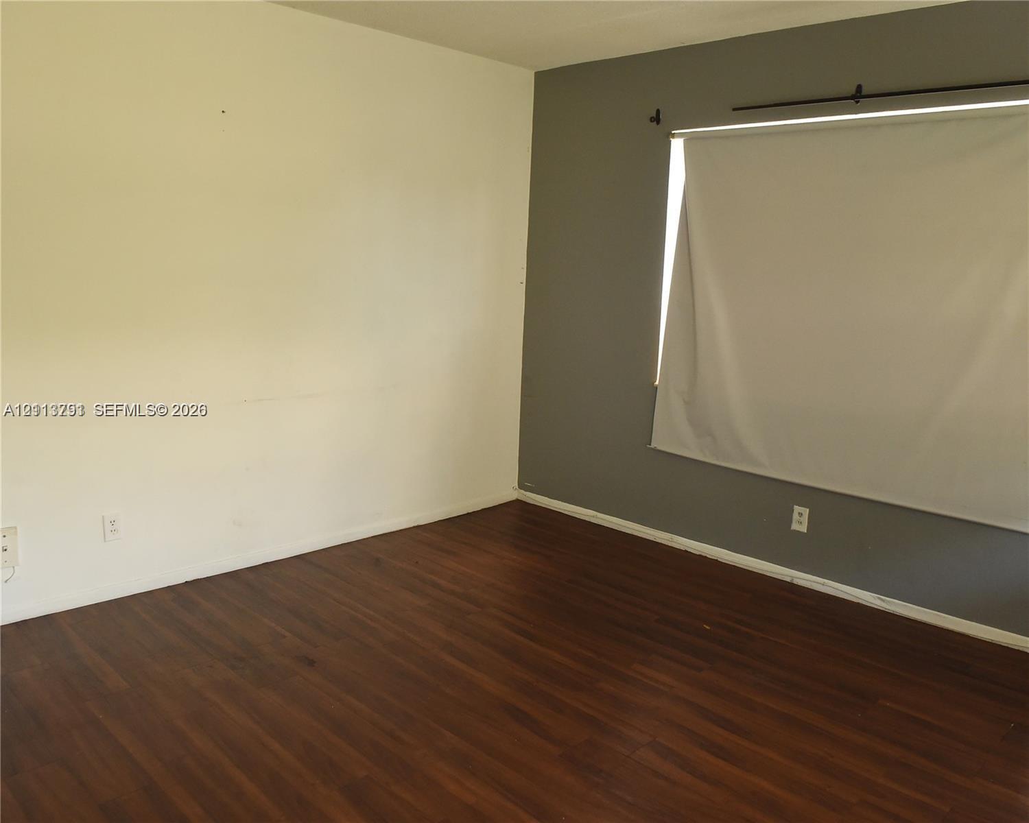 Room featuring dark wood-finish flooring, two-toned wall paint, and a horizontal window with a fitted roller shade