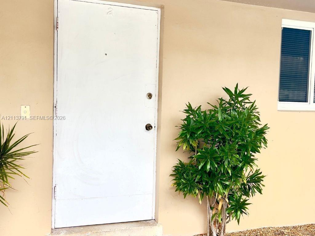 Solid white entry door with a peephole and metallic hardware, flush-mounted wall lighting, and a window with horizontal blinds Solid white entry door with a peephole and metallic hardware, flush-mounted wall lighting, and a window with horizontal blinds