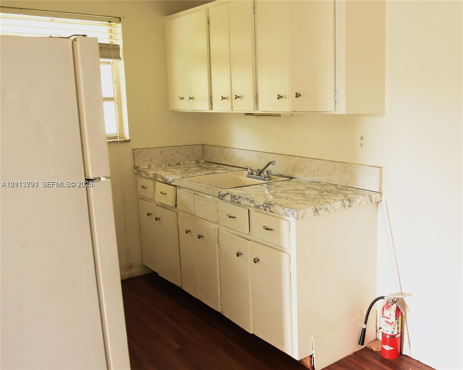 Kitchen featuring white cabinetry, patterned laminate countertops, a dual-basin sink with a metallic faucet, and wood-finish flooring Kitchen featuring white cabinetry, patterned laminate countertops, a dual-basin sink with a metallic faucet, and wood-finish flooring