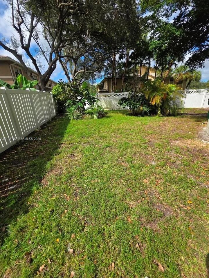 Backyard featuring a grass lawn, perimeter vinyl fencing, and mature trees