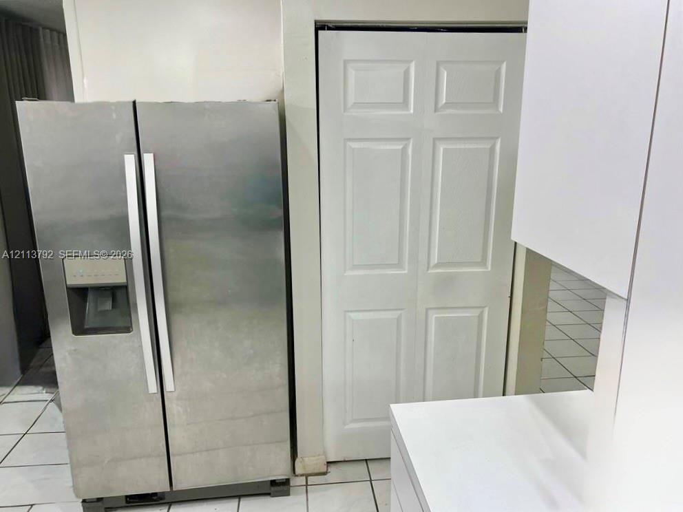 Stainless steel side-by-side refrigerator with exterior water and ice dispenser, complemented by white cabinetry and white tile flooring
