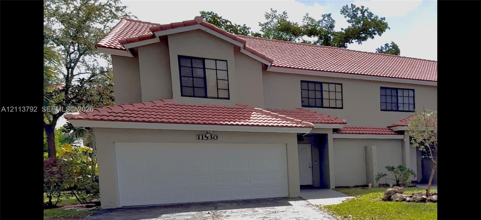 Two-story exterior featuring a terracotta-tiled roof, light-toned stucco facade, multi-pane windows, and an attached two-car garage Two-story exterior featuring a terracotta-tiled roof, light-toned stucco facade, multi-pane windows, and an attached two-car garage