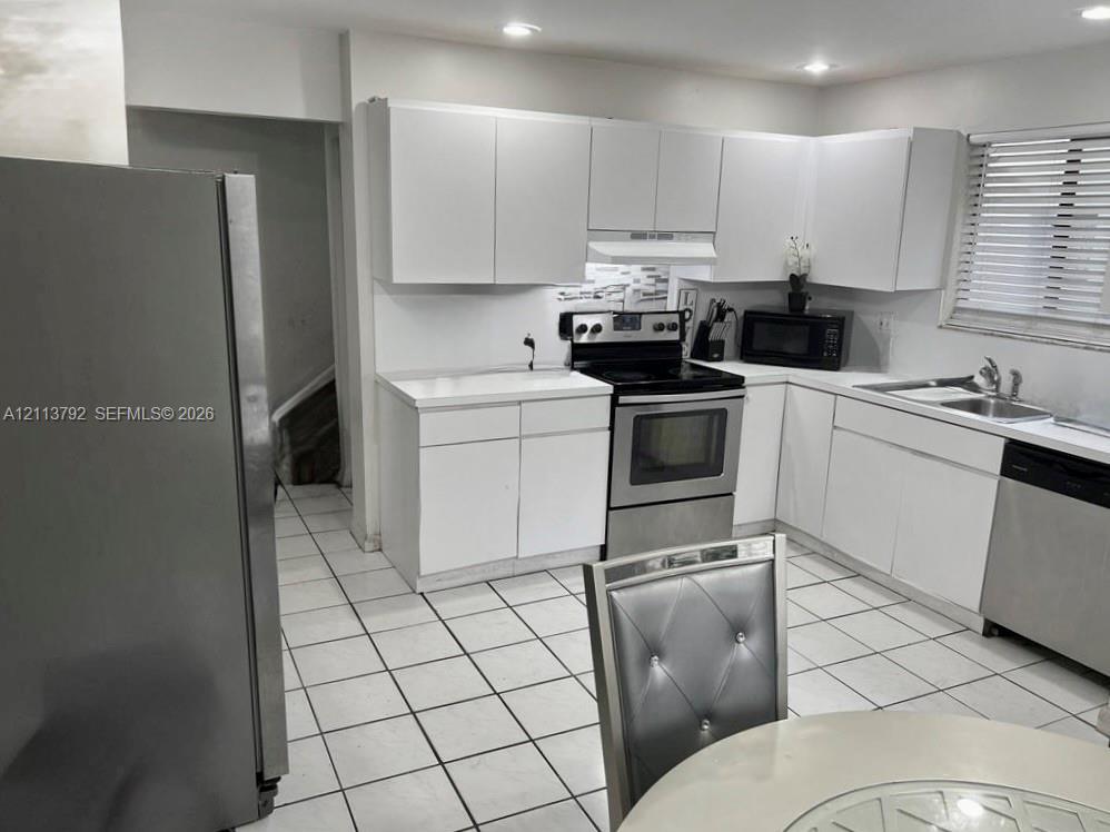 Kitchen featuring flat-panel white cabinetry, solid surface countertops, stainless steel appliances, ceramic tile flooring, and recessed lighting