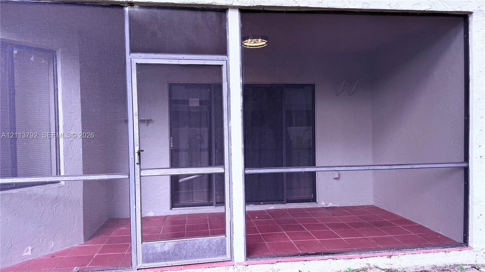 Screen-enclosed porch featuring tile flooring, textured wall finishes, and a ceiling-mounted light fixture