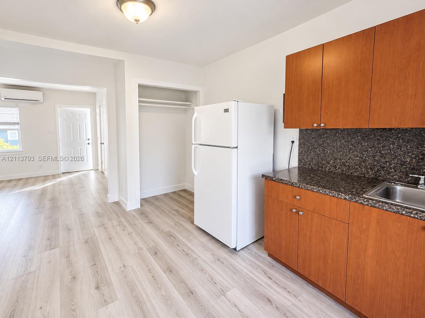 Kitchenette featuring wood-finish cabinetry, stone-texture countertops, an integrated stainless steel sink, and wood-finish flooring Kitchenette featuring wood-finish cabinetry, stone-texture countertops, an integrated stainless steel sink, and wood-finish flooring