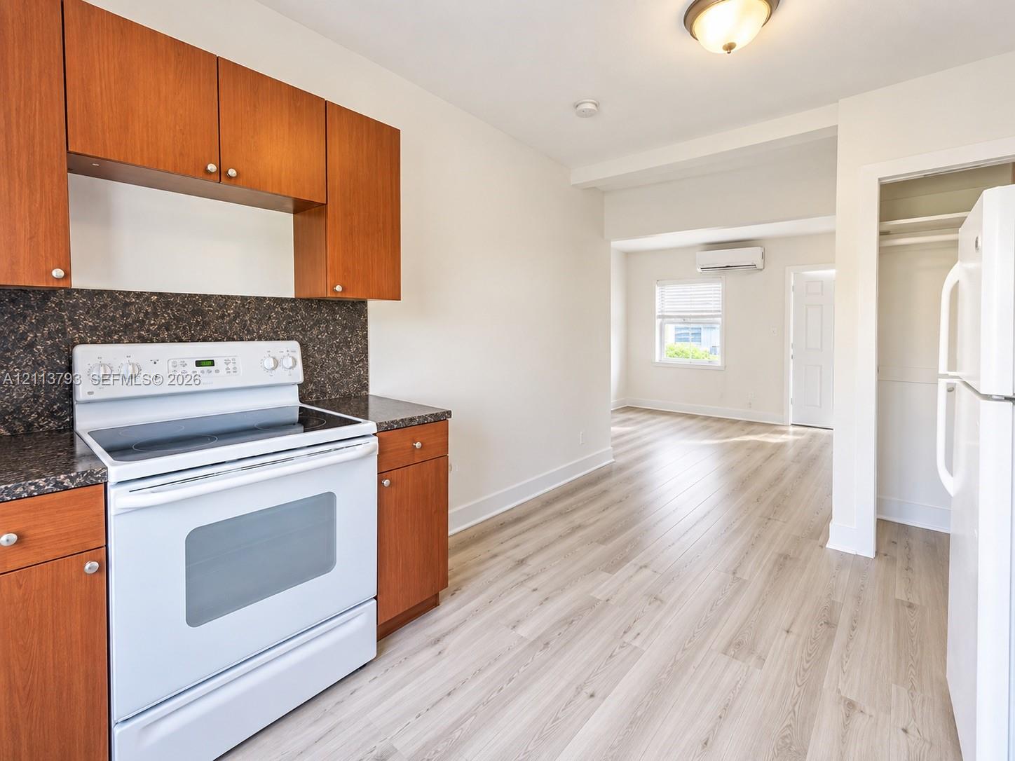 Kitchen area featuring wood-finish cabinetry, a white electric range, dark stone-style countertops, and wood-finish flooring Kitchen area featuring wood-finish cabinetry, a white electric range, dark stone-style countertops, and wood-finish flooring