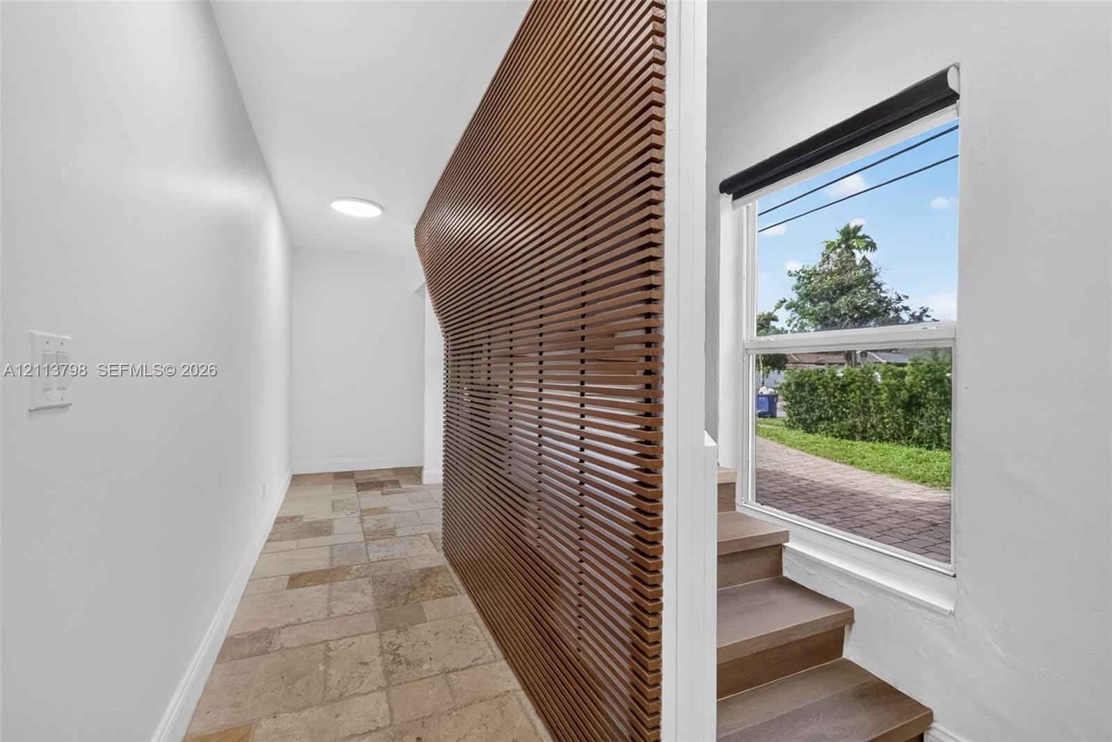 Interior featuring a curved slat-wood wall partition, large-format stone tile flooring, and stairs with wood-finish treads beneath a single-hung window