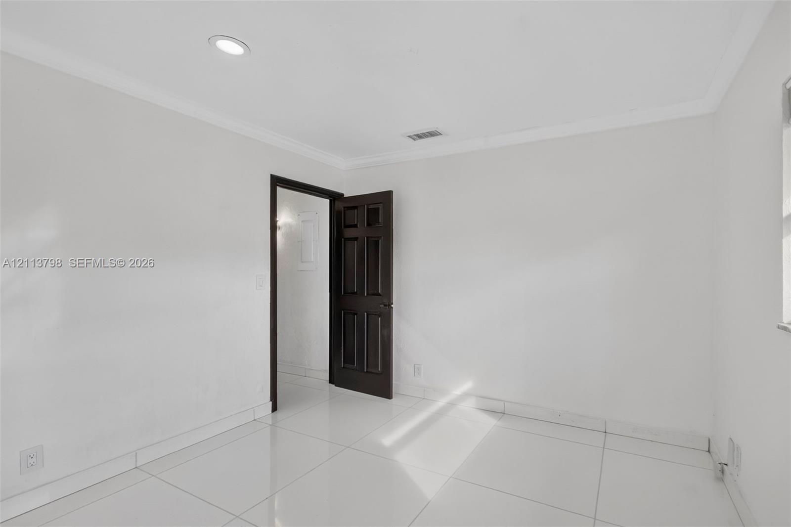 Interior room featuring large-format tile flooring, crown molding, recessed lighting, and a six-panel dark wood-finish door