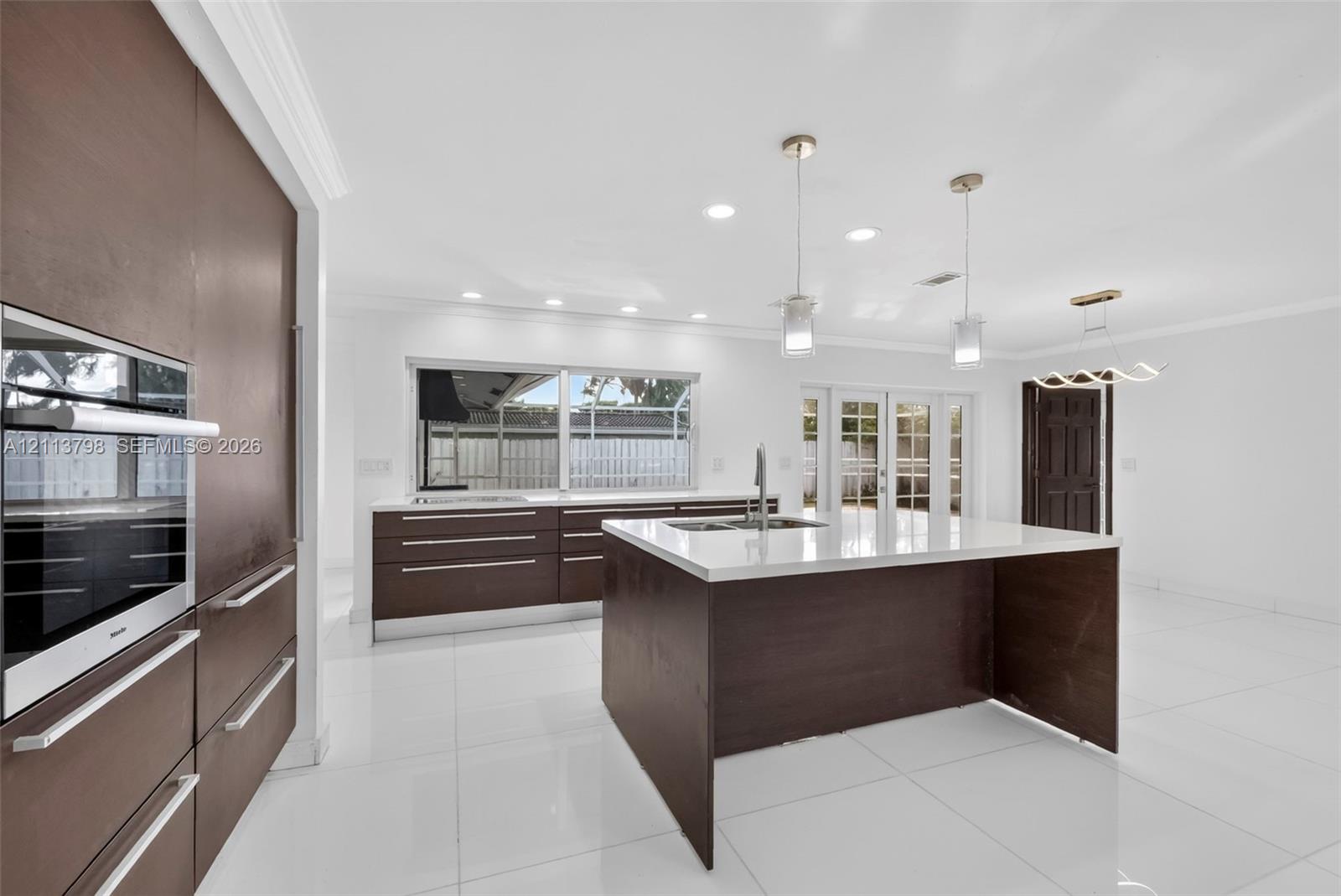 Kitchen featuring flat-panel cabinetry, a central island with a solid-surface countertop, recessed ceiling lighting, pendant light fixtures, and polished tile flooring Kitchen featuring flat-panel cabinetry, a central island with a solid-surface countertop, recessed ceiling lighting, pendant light fixtures, and polished tile flooring