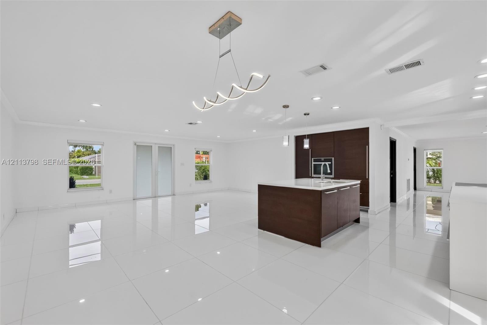 Open-concept interior featuring large-format tile flooring, a center island with a stone countertop, dark wood-finish cabinetry, recessed lighting, and a modern sculptural chandelier Open-concept interior featuring large-format tile flooring, a center island with a stone countertop, dark wood-finish cabinetry, recessed lighting, and a modern sculptural chandelier