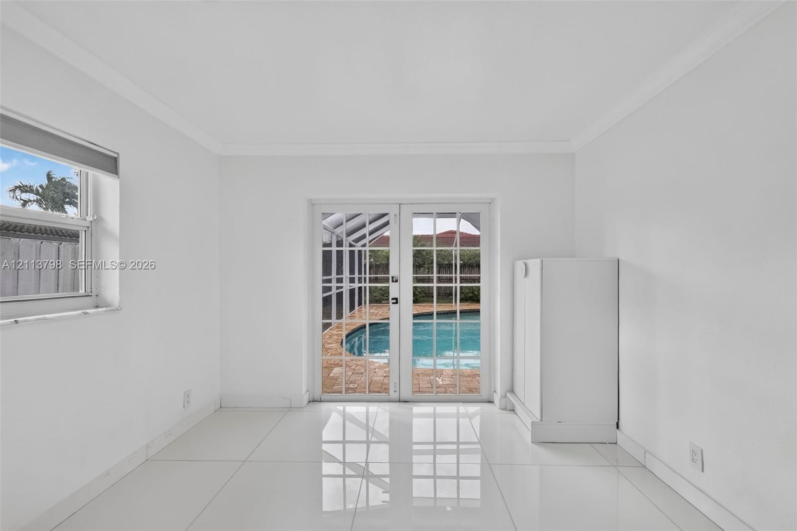 Interior space featuring white tile flooring, crown molding, double French doors, and built-in white cabinetry, with a perspective toward a screened pool enclosure