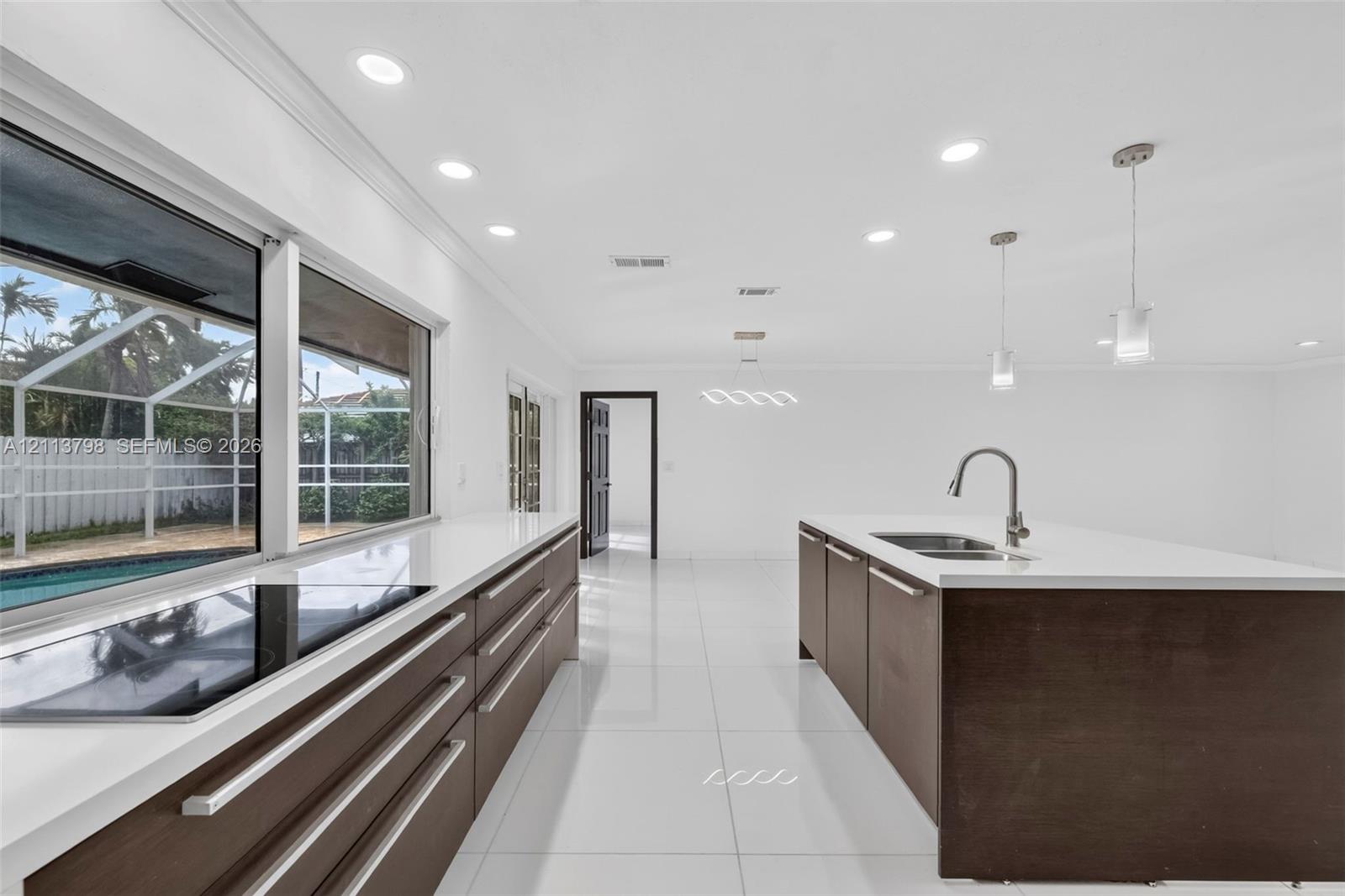 Kitchen featuring dark wood-finish cabinetry, solid-surface countertops, a center island with an undermount sink, porcelain tile flooring, and recessed lighting Kitchen featuring dark wood-finish cabinetry, solid-surface countertops, a center island with an undermount sink, porcelain tile flooring, and recessed lighting