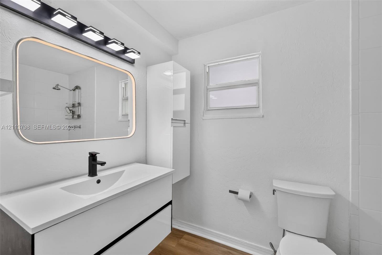 Bathroom featuring a floating vanity with a integrated basin, matte black faucet, wall-mounted storage cabinet, and large rectangular mirror with perimeter lighting