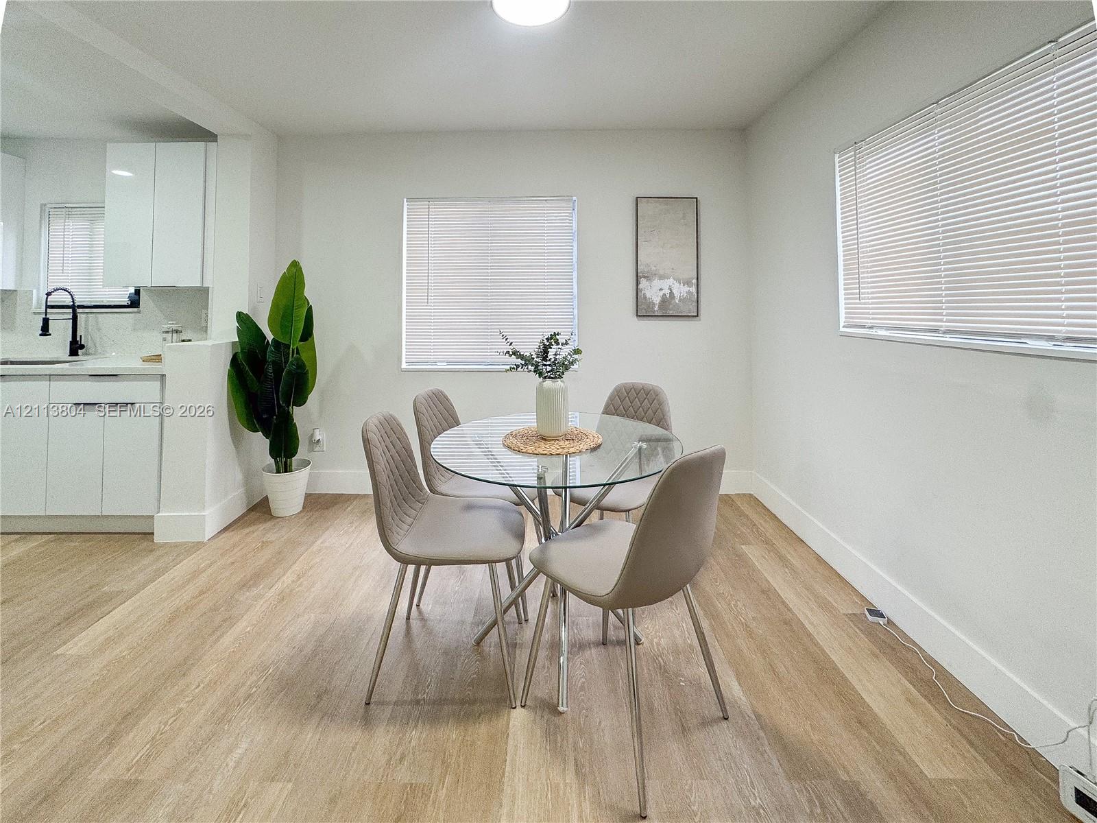 Bright interior space featuring wood-finish flooring, white cabinetry, integrated matte black fixtures, and multiple windows with horizontal blinds Bright interior space featuring wood-finish flooring, white cabinetry, integrated matte black fixtures, and multiple windows with horizontal blinds