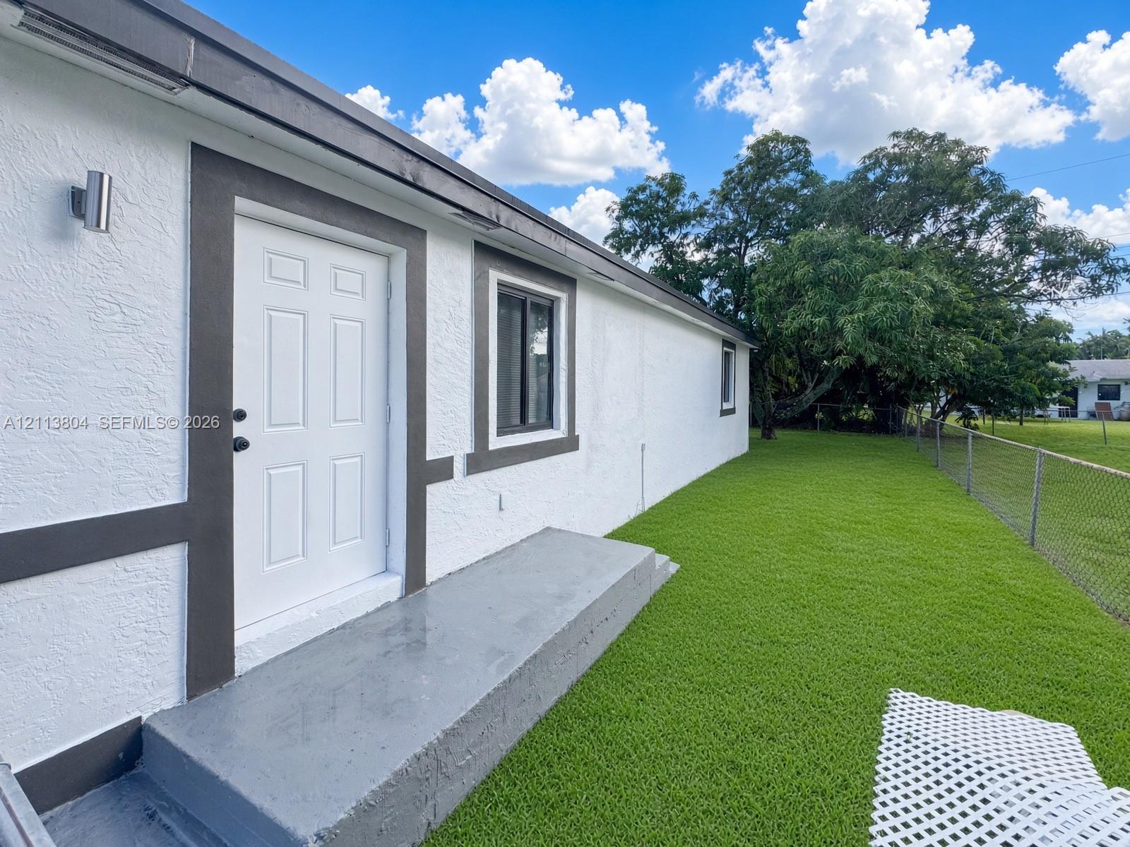 Exterior elevation featuring textured stucco siding, contrast trim, a concrete step, and a fenced-in grassy yard