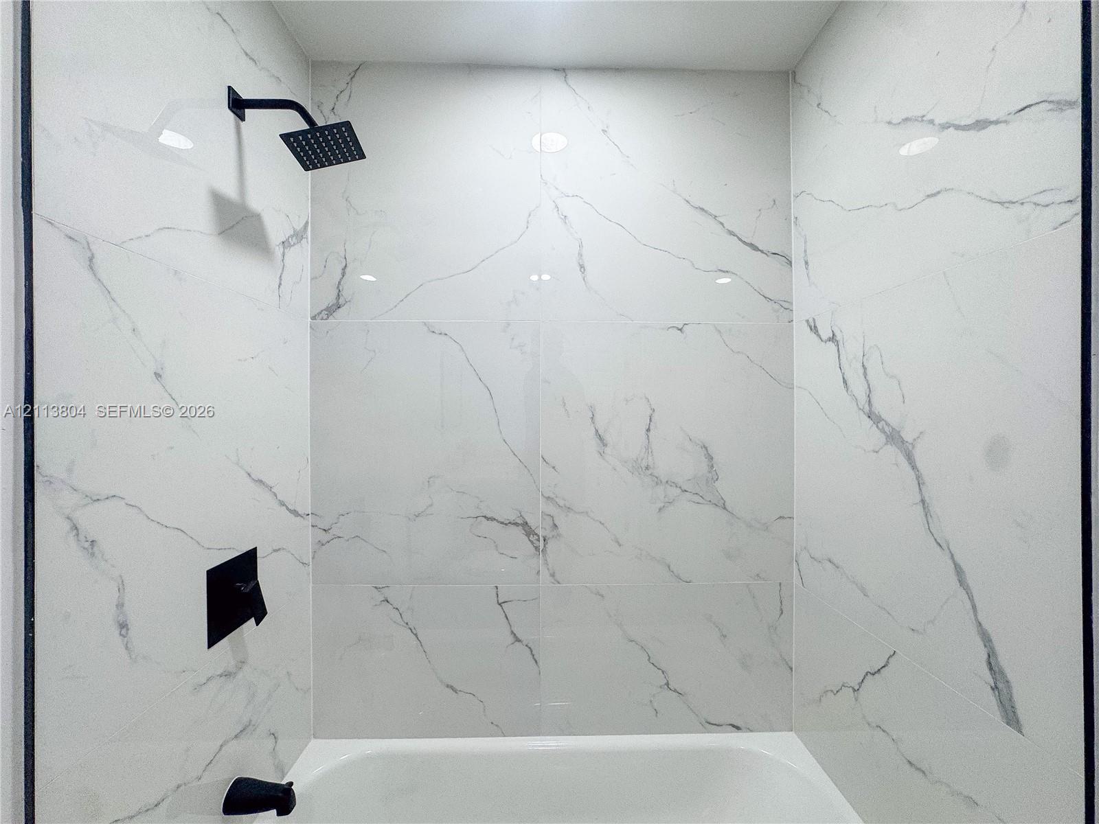 Shower area featuring large-format, veined tile wall surround, matte black rainfall showerhead, and matte black wall-mounted faucet controls