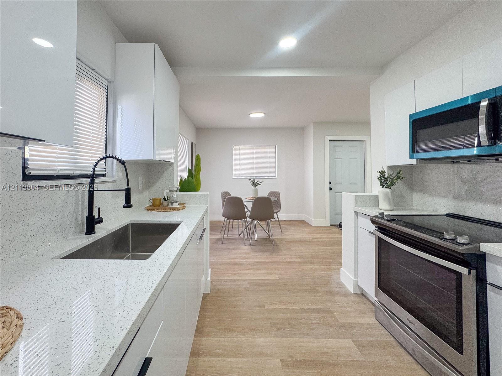 Kitchen featuring white slab cabinetry, light-toned stone-finish countertops, stainless steel undermount sink with a matte black faucet, and wood-finish flooring