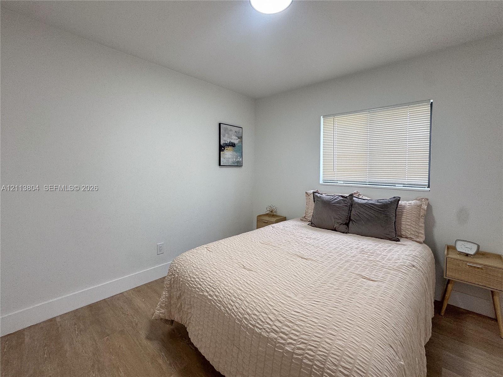 Neutral-toned interior space featuring wood-finish flooring, white walls, and a window with horizontal blinds