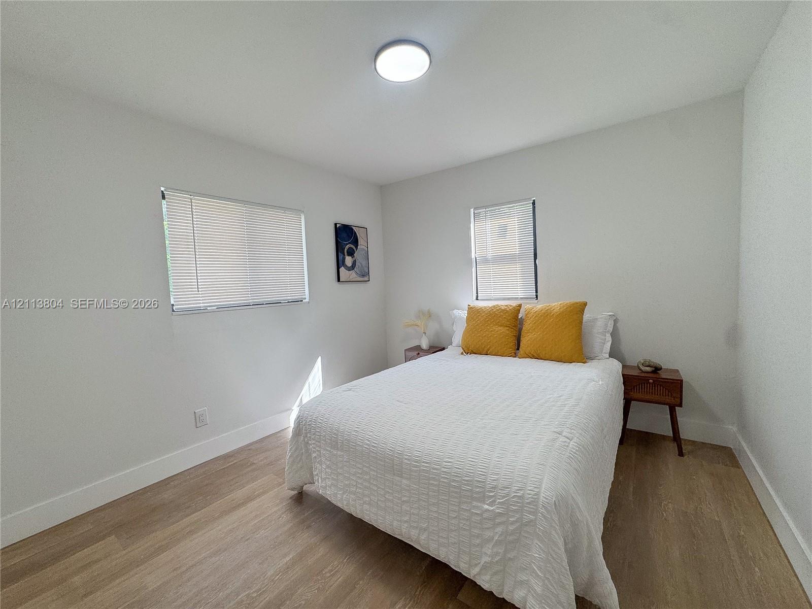 Neutral interior featuring wood-finish flooring, white walls, flush-mount lighting, and dual windows with fitted blinds