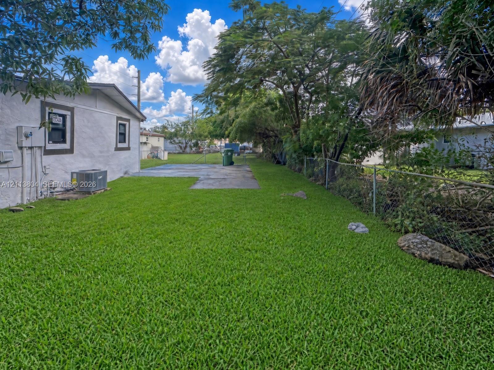 Backyard featuring a grass lawn, concrete patio, chain-link fencing, and mature trees
