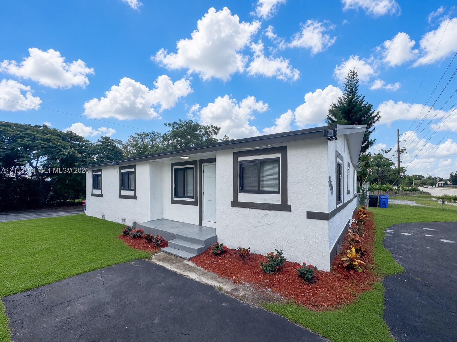 Exterior featuring white stucco siding with contrasting trim, a covered concrete front entry, and landscaped perimeter garden beds with mulch