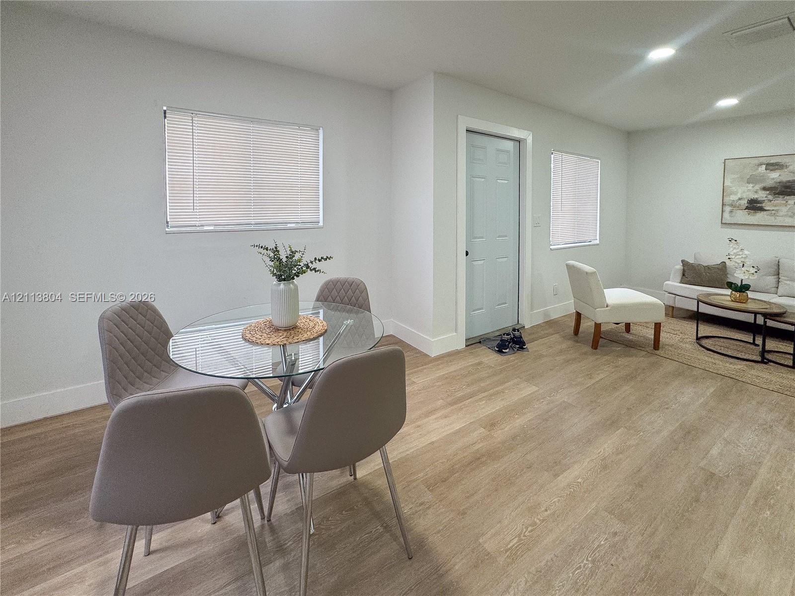 Open-concept interior featuring light wood-finish flooring, recessed lighting, neutral wall paint, and multiple windows with horizontal blinds Open-concept interior featuring light wood-finish flooring, recessed lighting, neutral wall paint, and multiple windows with horizontal blinds