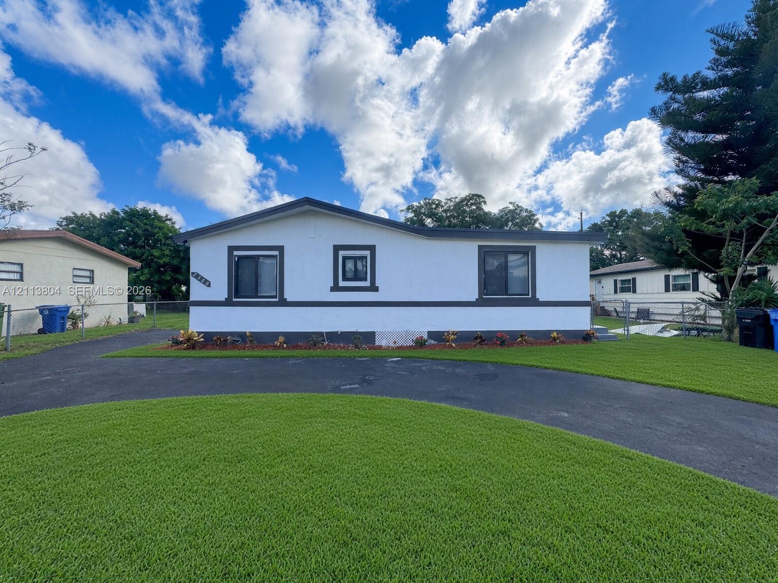 Single-story exterior featuring white stucco finish, contrasting dark trim, manicured lawn, and asphalt driveway Single-story exterior featuring white stucco finish, contrasting dark trim, manicured lawn, and asphalt driveway