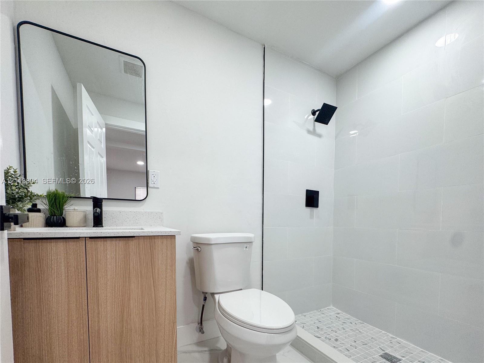 Modern vanity featuring light wood-finish cabinetry, a stone-composite countertop, and a rectangular mirror with a black frame