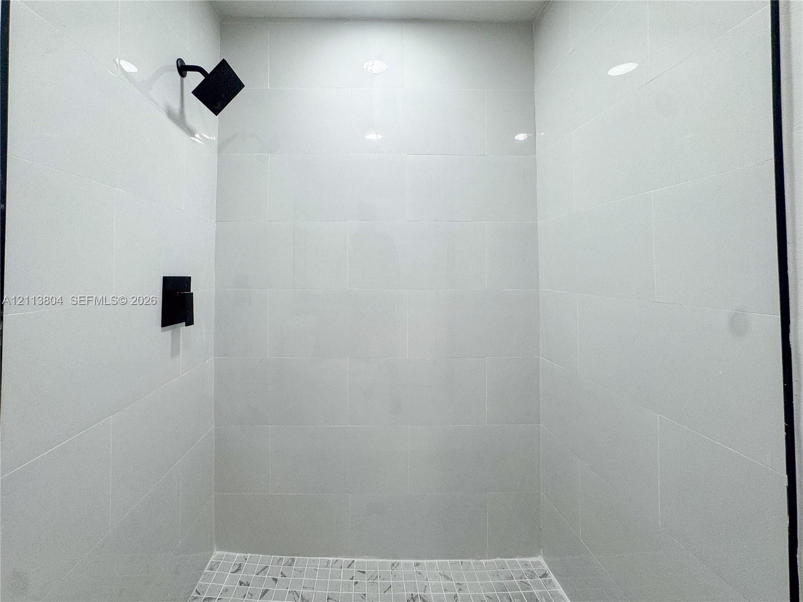 Walk-in shower enclosure featuring white subway tile wall surround, matte black rainfall showerhead, matte black pressure-balance valve, and a mosaic tile floor