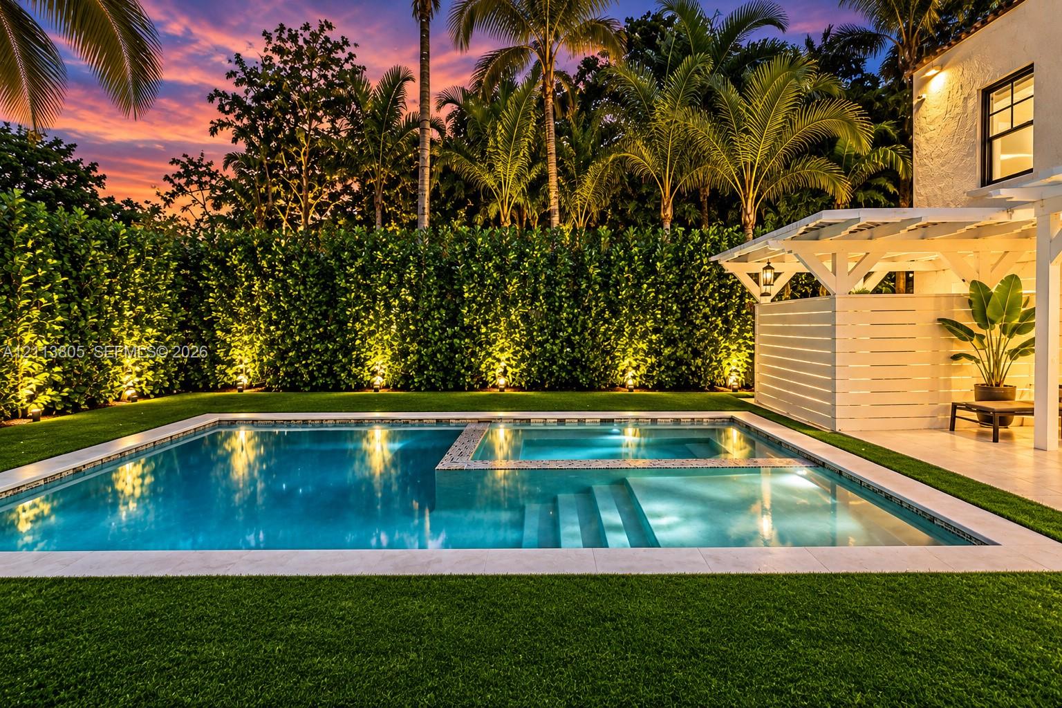 Outdoor pool with an integrated spa, stone coping, manicured turf, white pergola, and privacy hedging Outdoor pool with an integrated spa, stone coping, manicured turf, white pergola, and privacy hedging