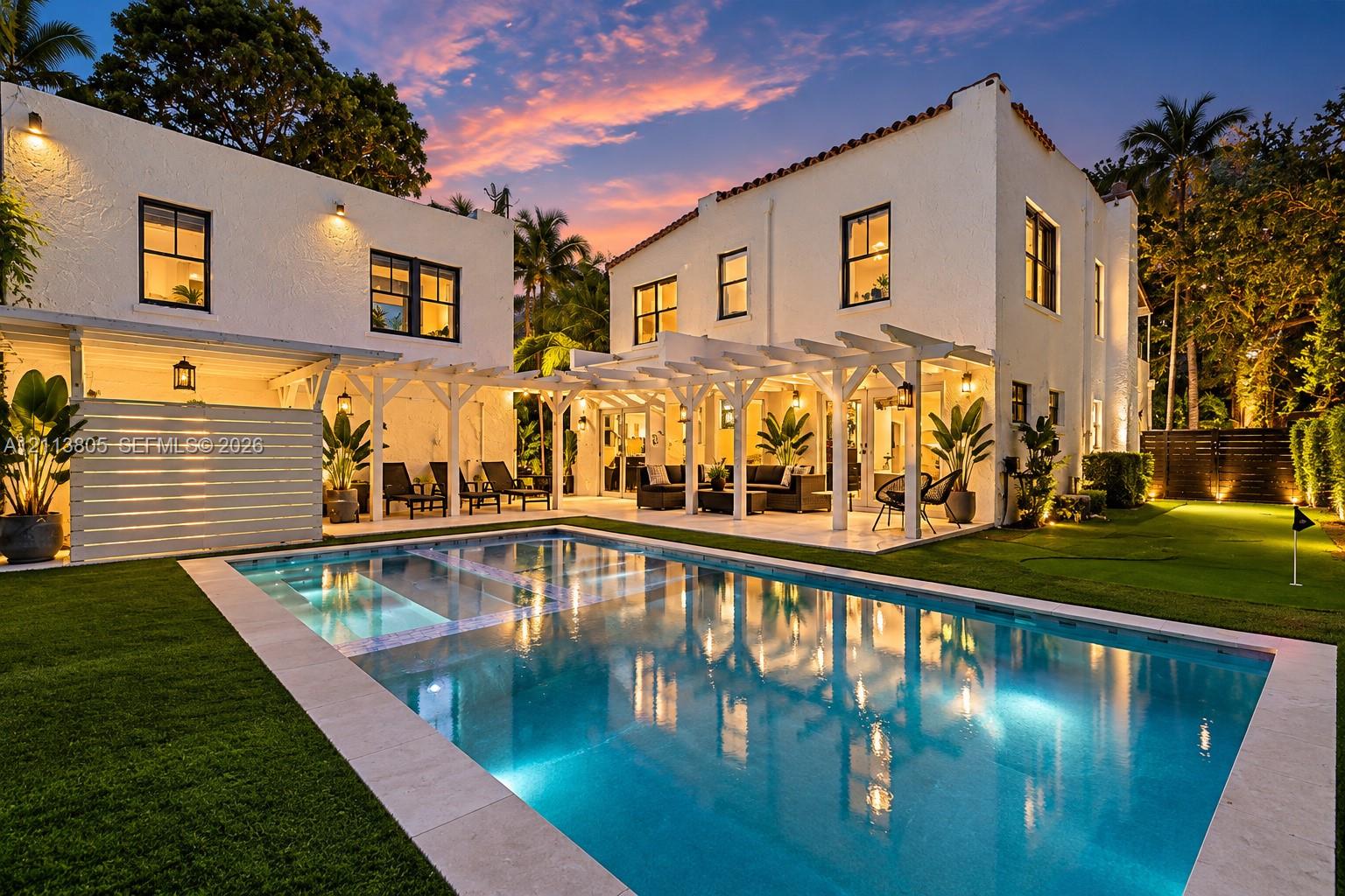 Stucco exterior featuring a dual-level layout, an expansive pergola-covered patio, a rectangular swimming pool with stone coping, and a synthetic turf lawn with an integrated putting green Stucco exterior featuring a dual-level layout, an expansive pergola-covered patio, a rectangular swimming pool with stone coping, and a synthetic turf lawn with an integrated putting green