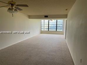 Expansive interior area featuring neutral wall-to-wall carpeting, a multi-blade ceiling fan with integrated light fixture, and large-scale windows with black frames