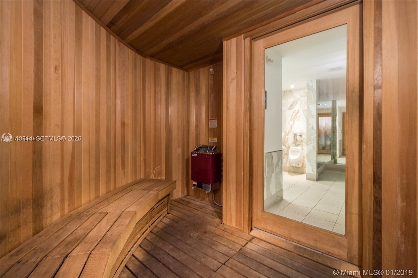Sauna featuring wood-plank walls, built-in wooden bench seating, slatted wood flooring, and a glass-panel door