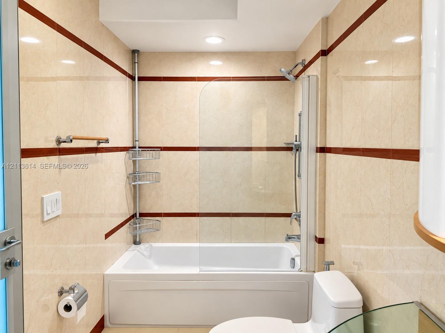 Bathroom featuring a full-sized bathtub with a glass splash panel, dual-finish wall tiling with integrated accent stripes, adjustable shower head, and recessed lighting