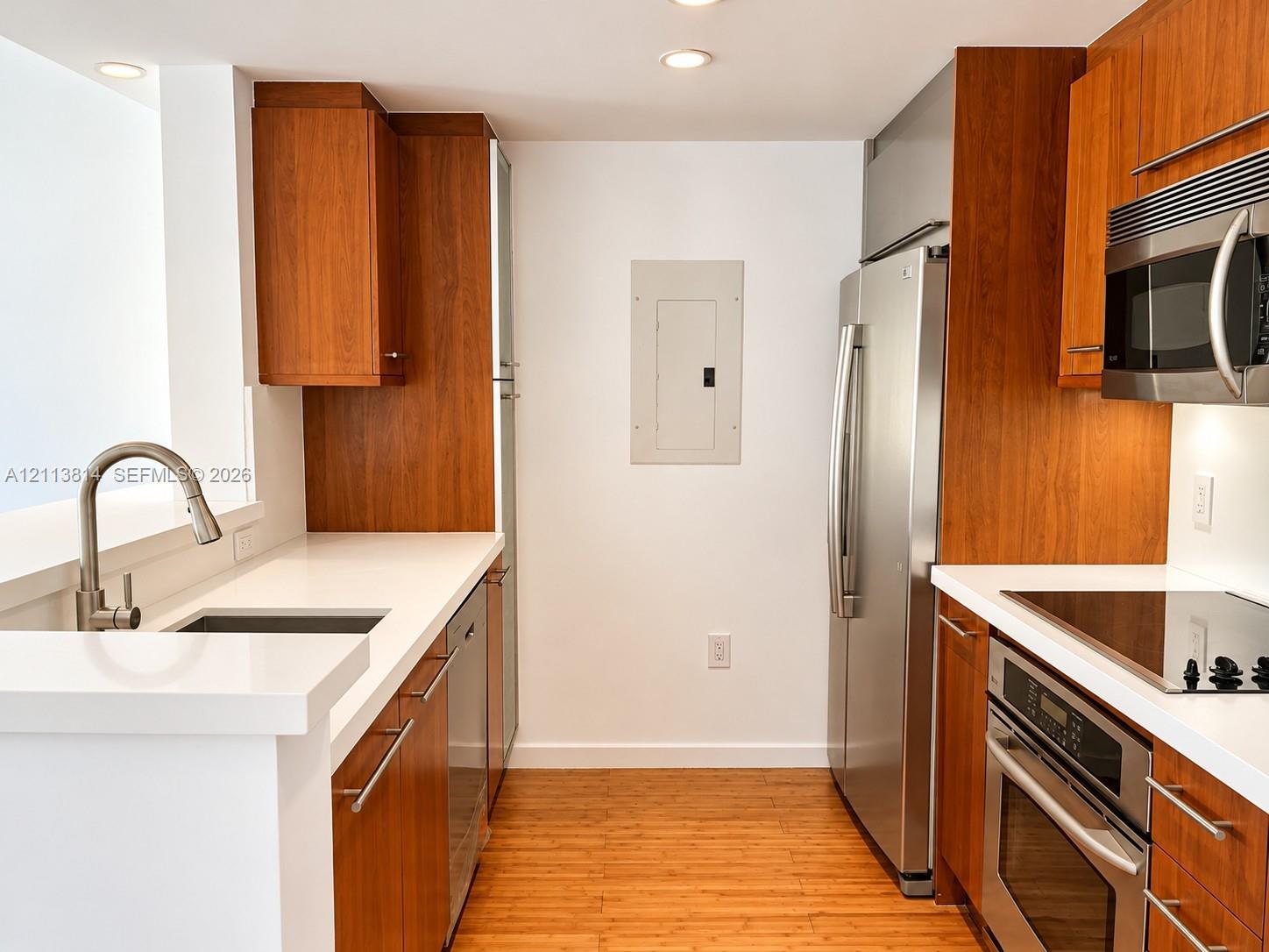 Kitchen featuring custom wood-finish cabinetry, solid surface countertops, stainless steel appliances, and wood-finish flooring