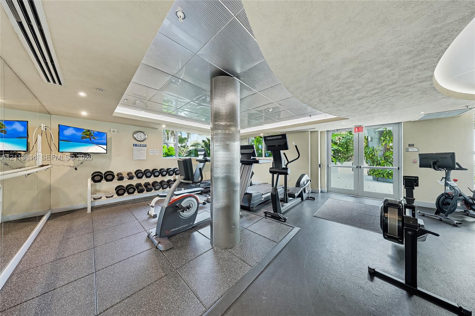Fitness center featuring large-format textured tile flooring, mirrored walls, and a recessed ceiling panel with metallic finish