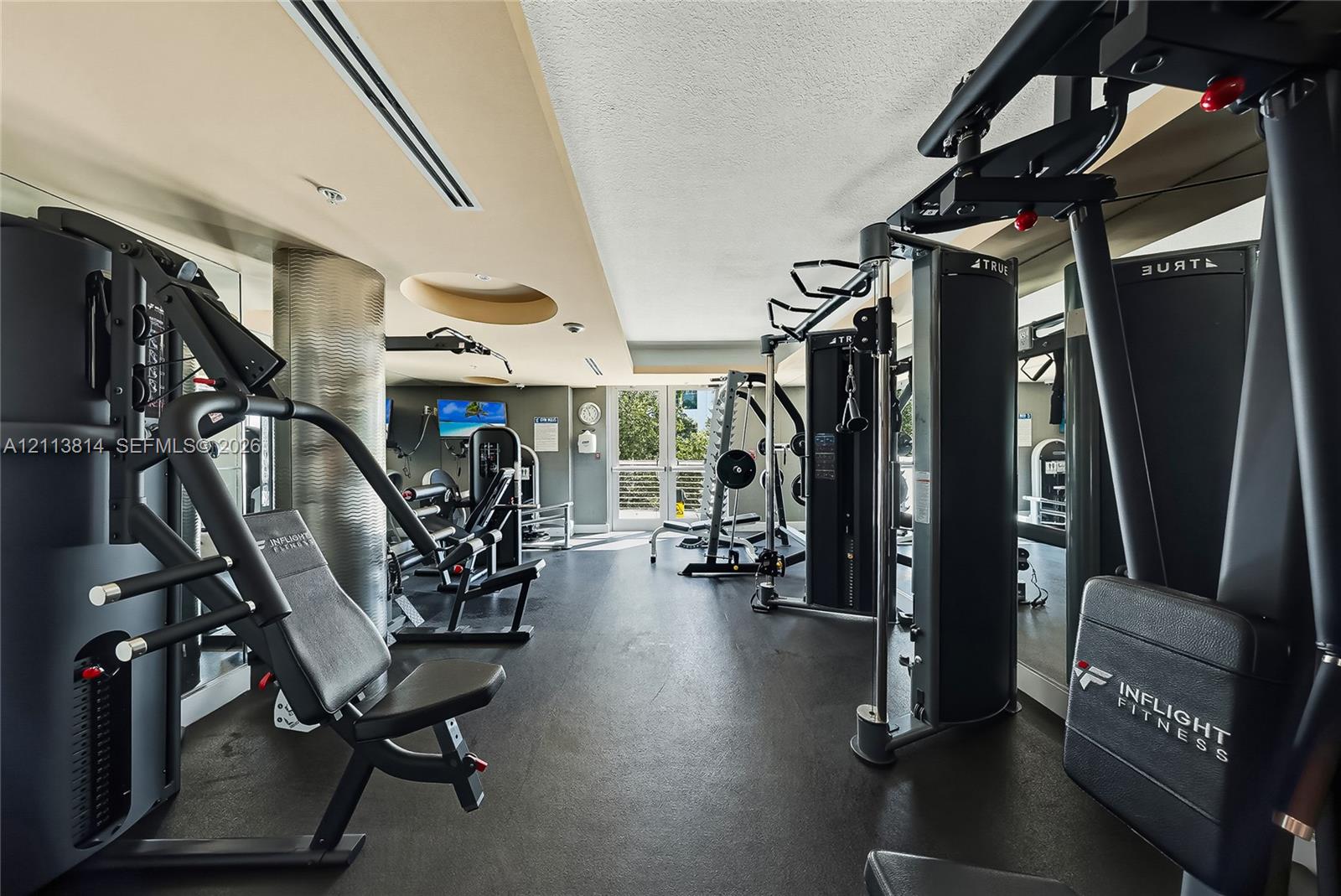 Fitness center featuring recessed ceiling lighting, a metallic cylindrical structural column, high-contrast wall finishes, and exterior-facing glass doors
