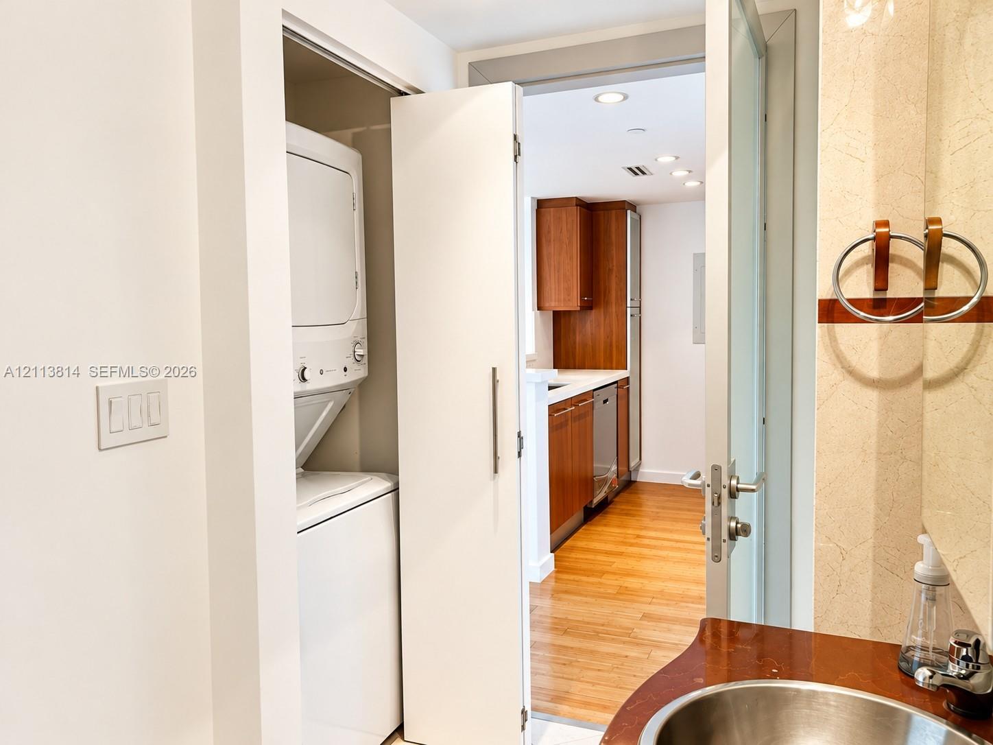 Enclosed laundry closet with stacked appliance unit, vanity featuring a metallic basin, and wood-finish flooring