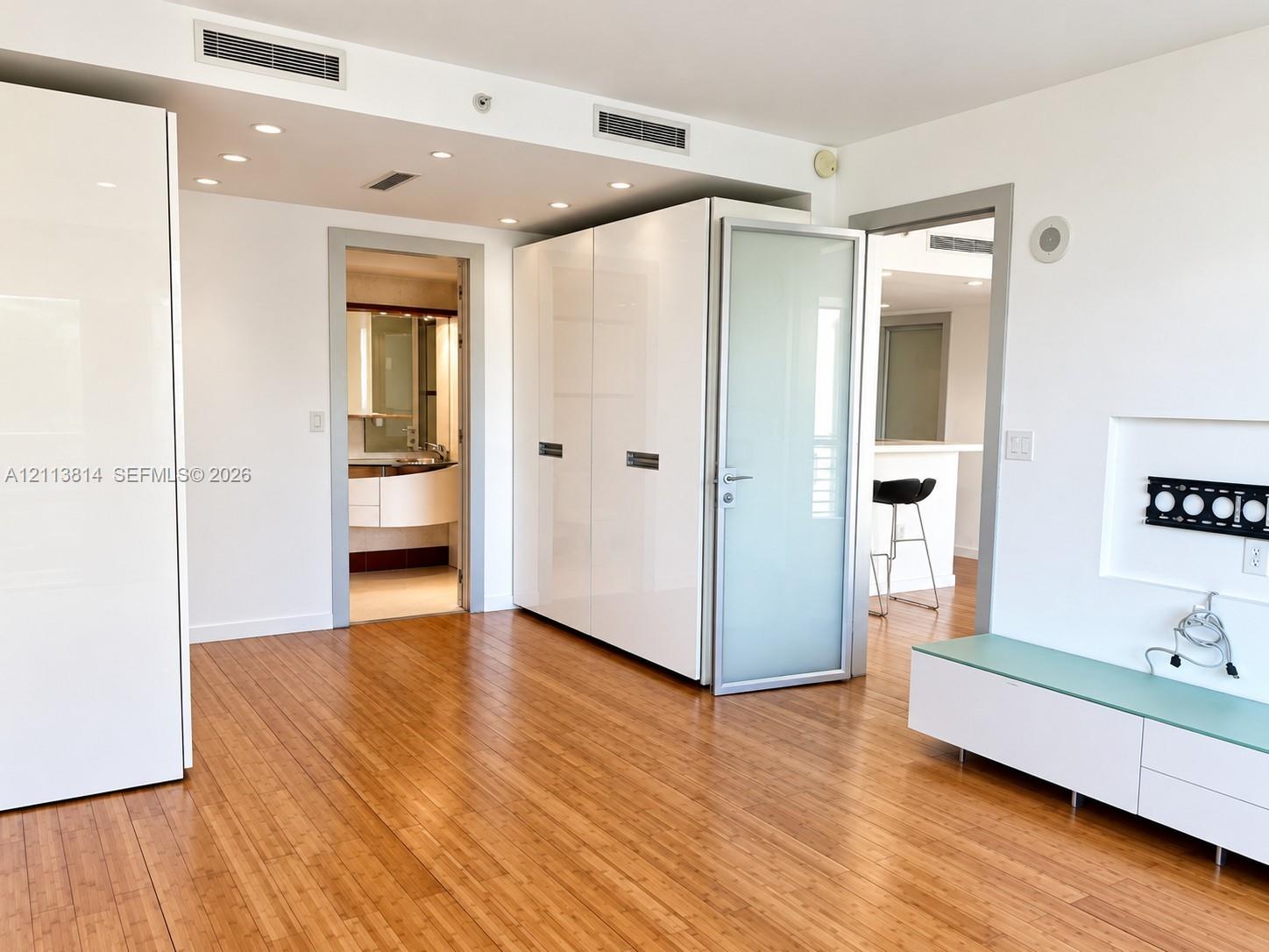 Interior space featuring light wood-finish flooring, high-gloss white built-in cabinetry, recessed ceiling lighting, and a frosted glass door with a metal frame