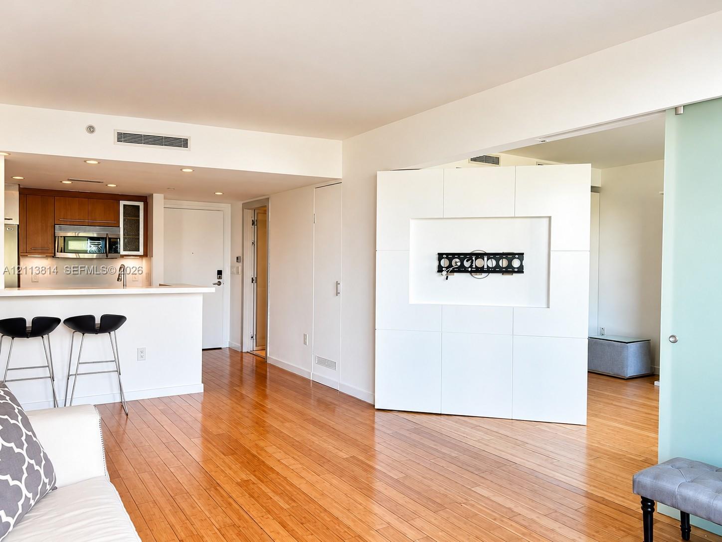 Hardwood flooring, wood cabinetry with stainless steel appliances, breakfast bar, recessed ceiling lighting, and a frosted glass sliding door
