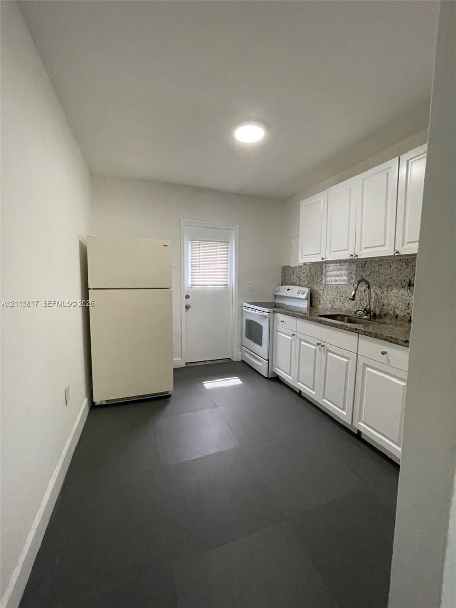 Kitchen featuring white cabinetry, stone-finish countertops, dark large-format tile flooring, a stainless steel sink with a high-arch faucet, and an exterior door
