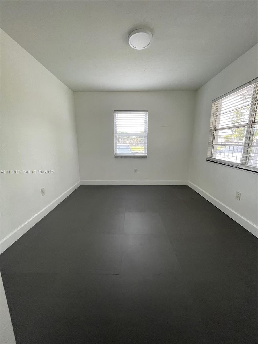 Neutral-toned interior space featuring dark grey tile flooring, bright white walls, two multi-pane windows with horizontal blinds, and a flush-mount ceiling light fixture